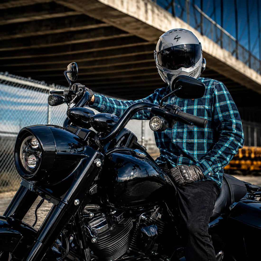 Rider on a customized, blacked-out cruiser motorcycle under an industrial overpass, showcasing the custom aesthetics and performance look.
