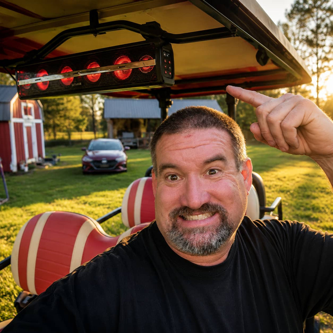 A happy off-road enthusiast taking a selfie in a custom golf cart, pointing up at a newly installed overhead golf cart soundbar with glowing red LED lights at sunset.