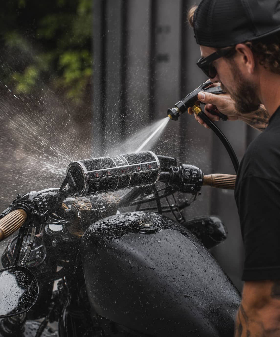 Man washing a motorcycle with a high-pressure hose, showing the KSPEAKER waterproof Bluetooth speaker enduring the water spray.